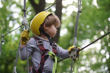 Güzel bir okul çocuğu macera parkında güneşli bir günün tadını çıkarıyor. Yüksek ipler yürür. Çocuk parkta oynuyordu. Tasasız çocukluk. Yürüyen çağ.