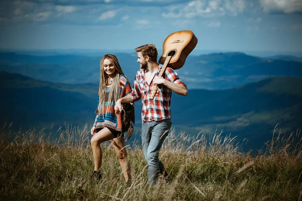 Sladká harmonie v horách. Šťastný pár cestovatelů mají procházku, úsměv a hrát na kytaru. — Stock fotografie