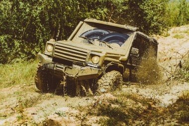 Dağların arasında bir kamyonet. 4x4 yolculuk gezisi. Jeep su birikintisine çarptı ve toprak püskürttü. Aşağıdan büyük off-road araba tekerleği kır yolu ve dağ zemininde
