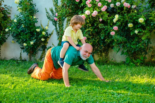 Old father play with son - happy fathers day, Fathers day. Happy senior man father with cute little boy son playing and looking at camera.