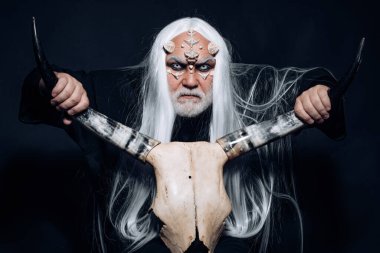 Şeytan korku konsepti. İki kırmızı boynuz tutan yaşlı bir adam. Beyaz mavi gözlü canavar. Boynuzlu kafalı bir Viking. Ejderha derisi ve gri sakallı bir uzaylı. Kötü vampir adam..