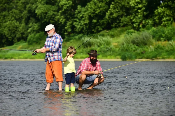Отец учит своего сына ловить рыбу, глядя на реку и пейзаж. Рыбалка в реке. Летние выходные. Отец и сын рыбачат . — стоковое фото