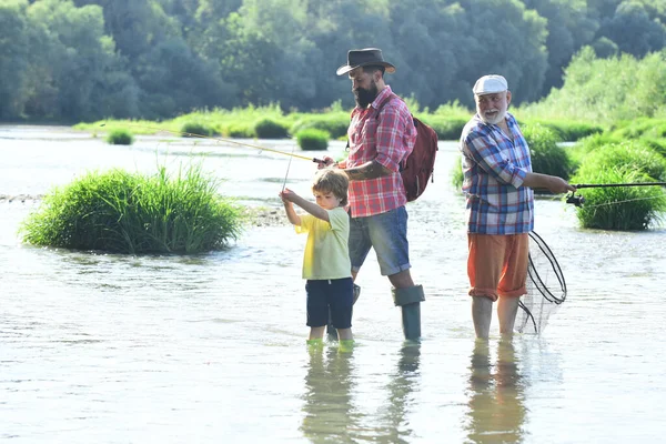 Buon nonno e nipote stanno pescando sul fiume. Padre, figlio e nonno in battuta di pesca. Uomo con il figlio e il padre sulla pesca fluviale con canne da pesca . — Foto Stock