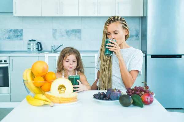 Filha e sua mãe feliz bebe smoothie verde. Refeição Vegan e menu de desintoxicação. Mãe e filha bebendo smoothie verde na cozinha. Alimentos orgânicos e vitamina para a família . — Fotografia de Stock