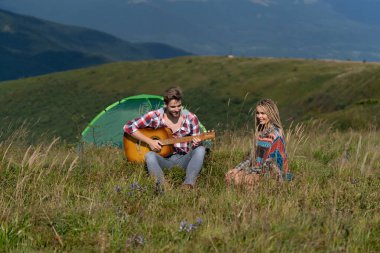 Kampta çim üstünde aşk çifti. Aşıklar doğanın tadını çıkarırlar. Birbirine aşık bir çift. Şehvetli kadın ve erkek. Sevgililer dışarıda sevişir. Kız arkadaş ve erkek arkadaş birlikte. Gitarlı mutlu kız ve oğlan.