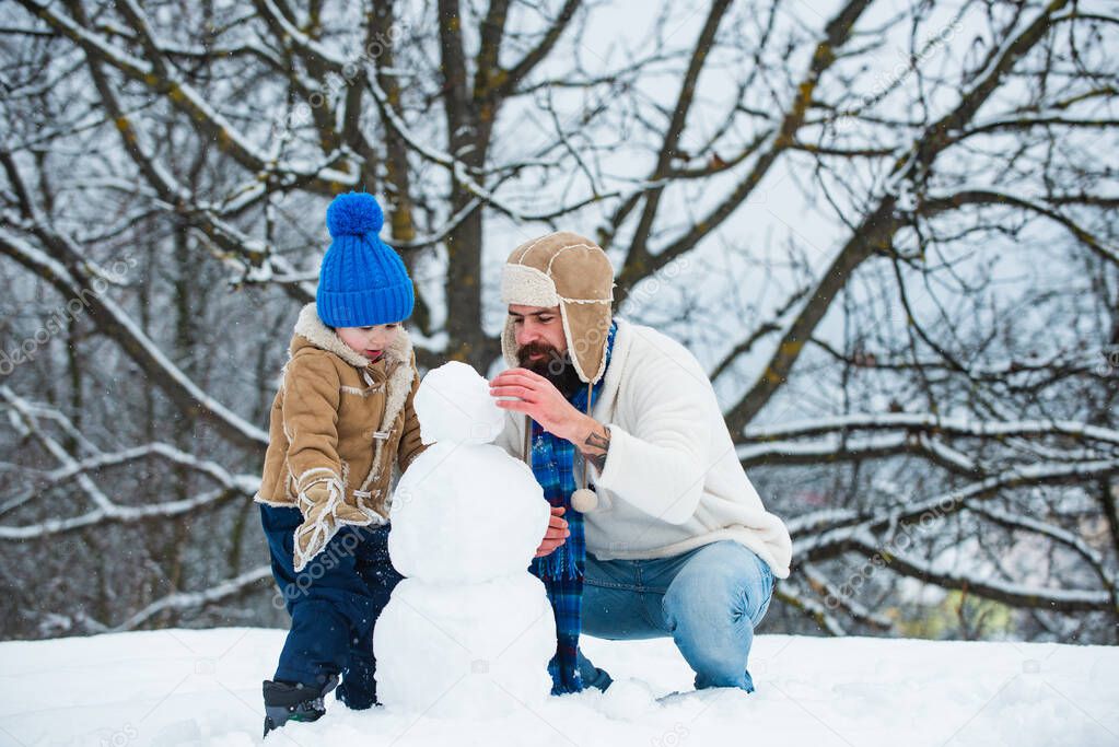Best winter game for happy family. Father and son making snowman. Winter background with snowflakes and snowman. Cute little child boy and happy father on snowy field outdoor.