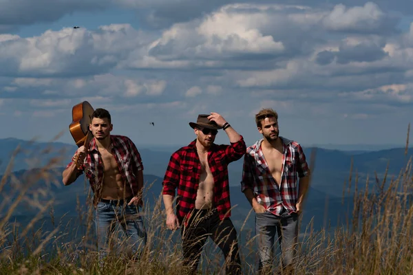 Μια ομάδα ανθρώπων με κιθάρα που περπατούν στα βουνά. Ομάδα ανθρώπων που κάνουν πεζοπορία στην ύπαιθρο. Τρεις νεαροί φίλοι σε μια βόλτα στην εξοχή. Ομάδα πεζοπόρους στην κορυφή του λόφου και απολαμβάνοντας θέα. — Φωτογραφία Αρχείου