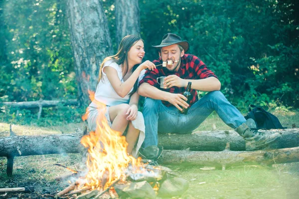 Weekend hike. Roasting marshmallows barbecue. Couple in love having a picnic. Funny couple roasting marshmallows on campfire. Happy couple in love on a camping trip relaxing by campfire.