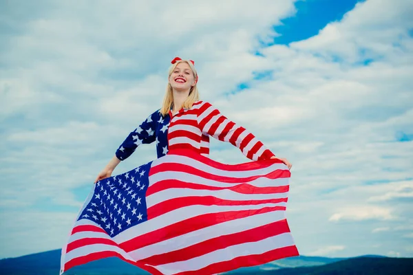 Happy woman holding USA flag. USA flag - woman showing american flag. Woman holding a waving American flag in American flagged clothes. Fourth of July.