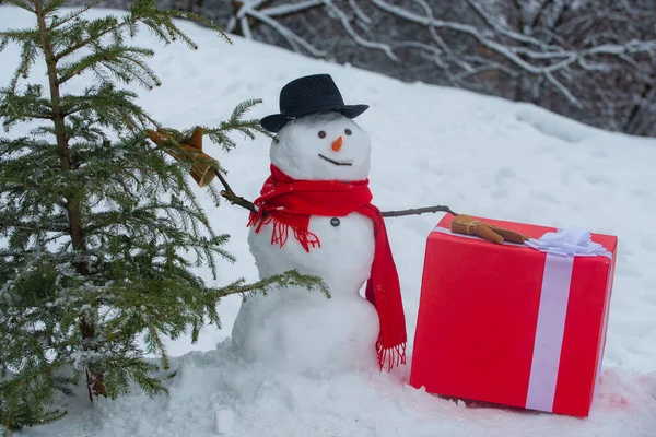 Sneeuwhouthakker met bijl in het winterbos. Snowman gaat een kerstboom kappen. Sneeuwman met bijl draagt kerstboom in het bos. Sneeuwman met vers gekapte kerstboom in — Stockfoto