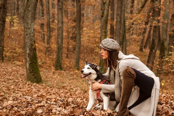 Mulher glamour na moda usando um chapéu e camisola cinza longa brincando com seu cão. Menina com seu animal de estimação relaxante lá fora. Fim de semana de outono. Modelo de outono. — Fotografia de Stock
