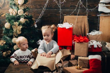 Yeni yıl çocukları. Ufaklık. Tahta arka planda Noel hediyesi olan bir çocuk. Kış çocukları. Noel ve yeni yılda hediyeleri açmak. Gülümseyen çocuk oturma odasında Noel ağacının arkasından dikizliyor..