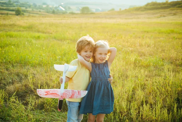 Smiling children having fun with toy airplane in autumn park. Smiling little couple walking over autumn field background. Sweet childhood. Summer portrait of happy cute children - sister and brother. — Stock Photo, Image
