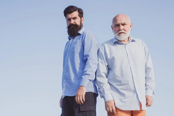 Handsome senior men in blue shirt. Male multi generation family walking. Portrait of two bearded men. Happy grandfather and father over blue sky and clouds background. — Stock Photo, Image