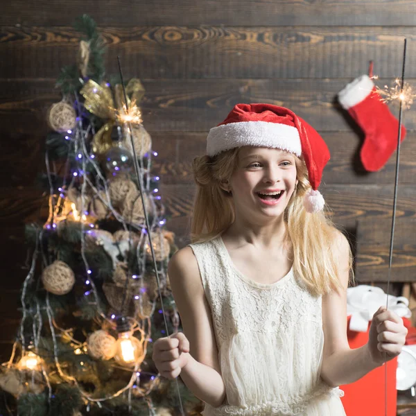 Vánoce zimní prázdniny koncept. Roztomilá holčička teenager zdobí vánoční stromeček uvnitř. Portrét dítě s dárkem na dřevěném pozadí. Novoroční děti. — Stock fotografie