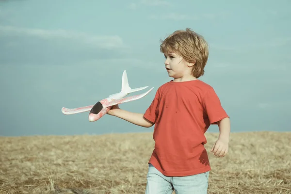 日没時に野外でおもちゃの飛行機を持つ小さな子供たち。成功と子供のリーダーの概念。パイロットになる夢を見る少年。晴れた夏の日に小麦畑を歩くかわいい子供. — ストック写真