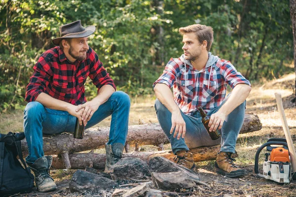 Two lumberjack men making picnic. Enjoying camping holiday in countryside. Happy young male friends having picnic. Company adult friends relaxing near campfire. Good day for spring picnic in nature.