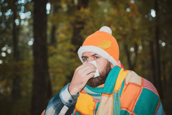 Przystojny hipsterz z brodą owinięty w wielokolorowy koc, noszący ciepły kapelusz, cieknący nos. Koncepcja odporności na choroby sezonowe, przeziębienia, zapobieganie katar, alergia. — Zdjęcie stockowe