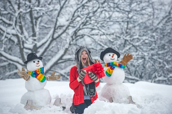Holly alegre botín de Navidad y Noel. Mujer feliz retrato de invierno. Hombre de nieve. Retrato de invierno de la joven hermosa mujer en la nieve Jardín hacer muñeco de nieve . — Foto de Stock