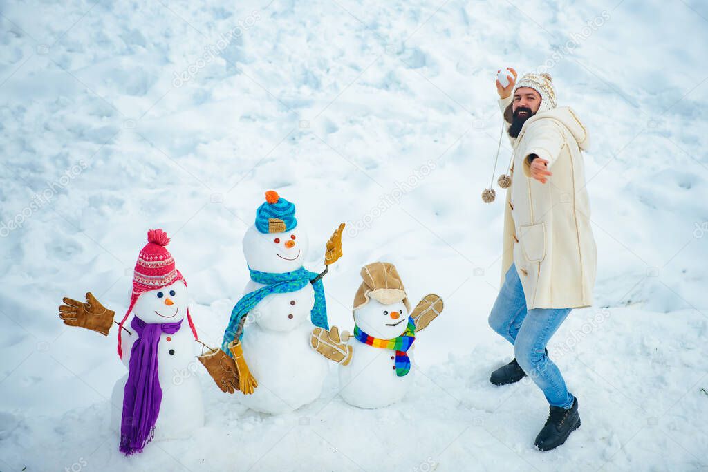 Young hipster winter portrait. Christmas preparation - funny bearded man make snowman. People in snow. Snowman. Funny winter people Portrait.