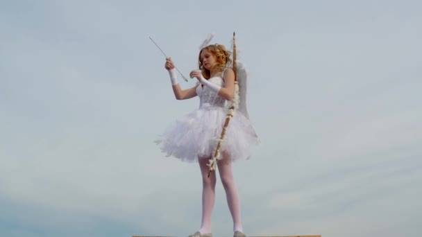 Cupid cute girl with a bow. Cherub girl. arrow and wings. Little girl with angel wings and halo. Little angel girl against sunny sky. — Stock Video