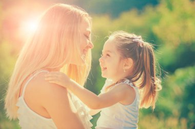 Çocuklar bayılır. Mutlu anne ve kız, arka planda sarılıyorlar. İnsanlar mutluluk ve sevgi. Küçük kızıyla birlikte gün batımında gülümseyen mutlu anne portresi..