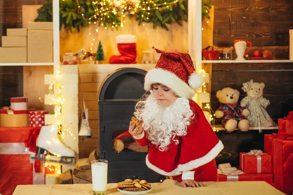 행복 산타 클로스 - 귀여운 소년 아이가 쿠키를 먹고 집에서 우유 의 유리를 마시는 크리스마스 인테리어. 집에서 작은 산타 따기 쿠키와 우유 한 잔. — 스톡 사진