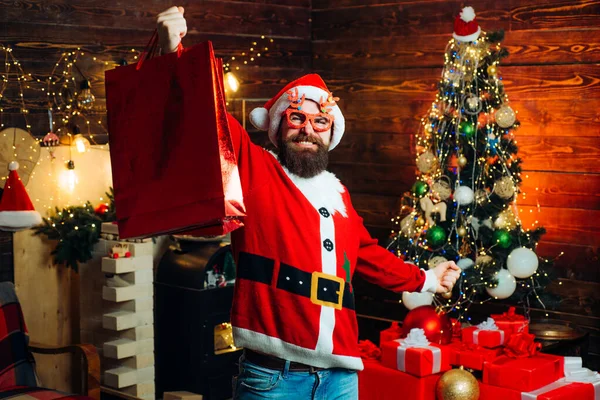 Hipster in rode Kerstman hoed met boodschappentas. Nieuwjaarsconcept. Huiselijke kerstsfeer. Hipster Santa thuis. Nieuwjaar Kerstconcept. Gelukkig nieuwjaar. — Stockfoto