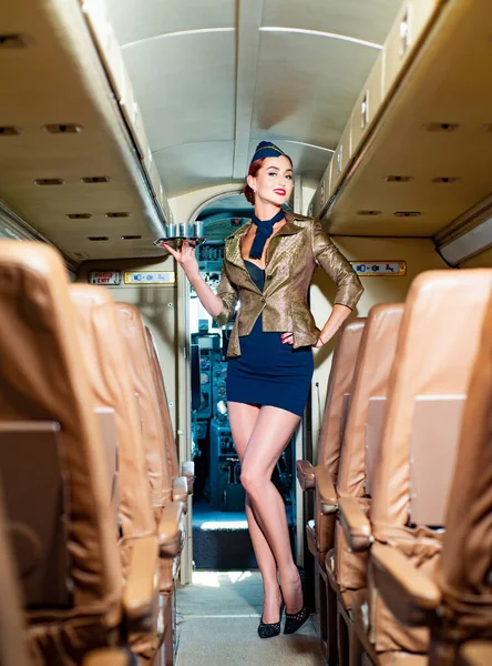 Mooie charmante stewardess gekleed in officieel blauw uniform verblijft in het vliegtuig in de luchthaven. Portret van charmante stewardess in blauw uniform. Lifestyle en reizen. — Stockfoto