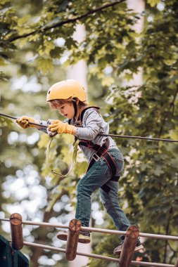 Ağaçların arasındaki halat parkındaki güzel bir çocuğun portresi. Mutlu çocuk yüksek ağaca ve halatlara tırmanırken arıyor. Eko Tatil Köyü Eylemleri