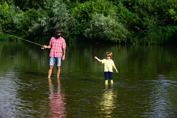 Маленька рибалка-помічник. Риболовля батька та сина - сімейний час разом. Батько і син рибалять і розслабляються, насолоджуючись хобі. Щасливий батько і син з рибальськими палицями на річковому причалі . — стокове фото