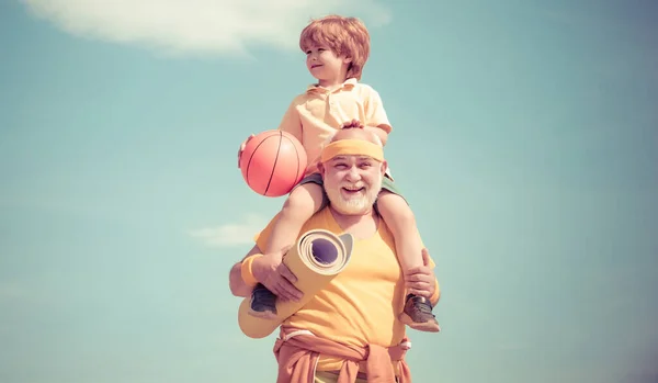 Different generations. Child sits on the shoulders of his grandfather. Outdoor activities and healthy lifestyle. Grandfather giving grandson ride on back in park.