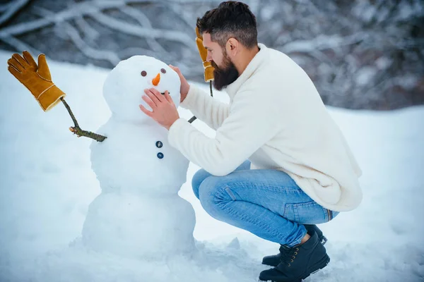 Snowman and funny bearded man in the snow. Man playing with Snowman - isolated on snow background. Joyful Handsome young hipster Having Fun with snowman in Winter Park. — Stock Photo, Image