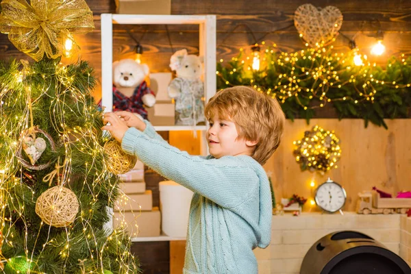 Szczęśliwe dziecko trzymające bombkę przed choinką. Mały chłopiec cieszy się z Nowego Roku. Przygotowanie świąteczne. — Zdjęcie stockowe