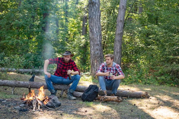 Young man having picnic in woods. Camp adventure and travel concept. Happy friends enjoying bonfire in nature. Group of two male friends camping with marshmallows over a camp fire.