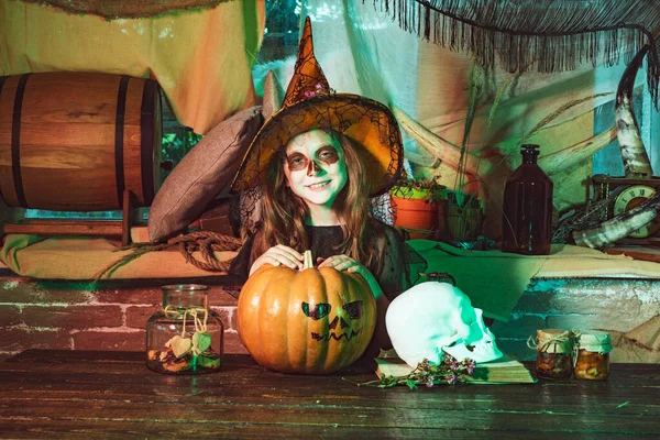 Niño divertido con calabazas y dulces. Feliz niña divertida con calabaza de Halloween hacer cara divertida. niña usando disfraz de Halloween con calabaza una vieja casa de madera . —  Fotos de Stock