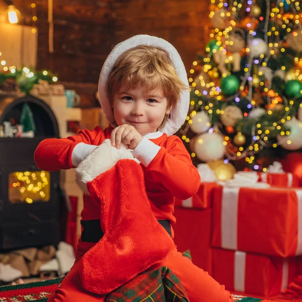 クリスマスのストッキング、かわいいサンタの男の子はクリスマスの靴下に存在を探しています。ギフトカードの概念。メリークリスマスと幸せな新年。クリスマスプレゼント新年の驚きのプレゼント。休日割引. — ストック写真