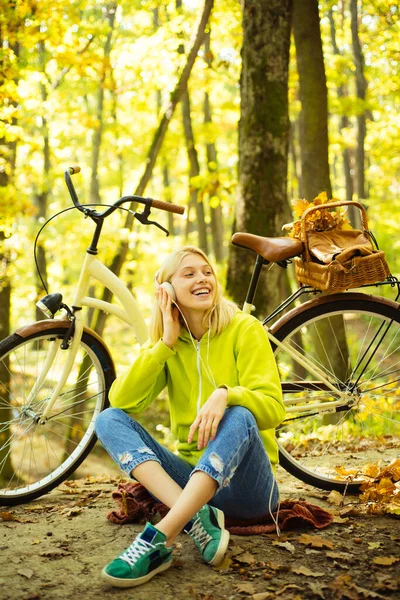 Joyful jonge college meisje ontspannen in het bos het dragen van groene kleren en luisteren bedachtzaam naar muziek in hoofdtelefoon. Actieve recreatie en levensstijl. Meisjesfiets voor de lol. — Stockfoto