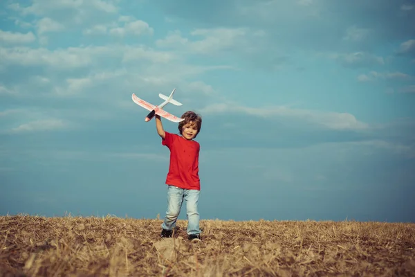 彼の手に飛行機で村の子供。自然を背景にレトロなスタイルの飛行機。おもちゃの飛行機で遊んでいる子供の男の子と夢の未来。子供の頃。コンセプト子供と自然. — ストック写真