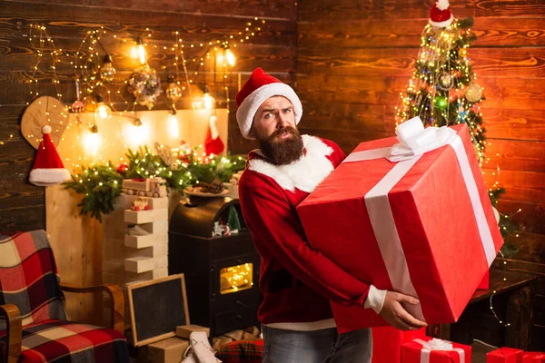 Hipster en Santa Sombrero rojo sosteniendo presente. Regalos de entrega. Emociones de regalo. Feliz Navidad y Felices Fiestas. Santa hombre sosteniendo regalo . —  Fotos de Stock