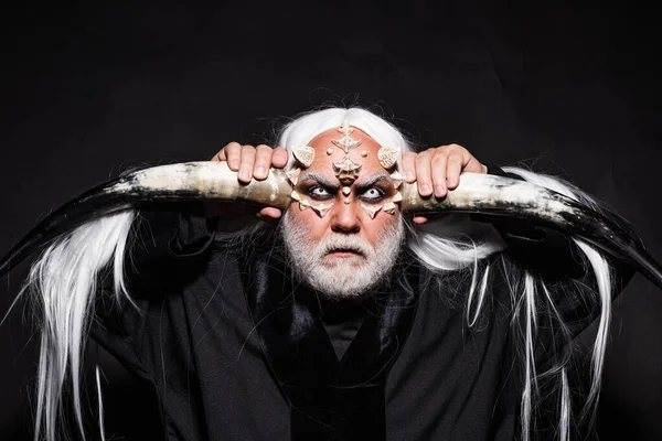 Viejo barbudo vestido como un monstruo de Halloween. Anciano sosteniendo dos cuernos rojos. Horror con el aterrador hombre de Halloween. Mago demonio hombre con piel de dragón y cuernos . — Foto de Stock