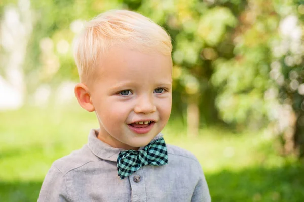 Jest szczęśliwy. Międzynarodowy Dzień Dziecka. Urocze dziecko dobrze się bawi. Chłopak w garniturze i muszce. Portret uśmiechniętego chłopca na tle natury. — Zdjęcie stockowe