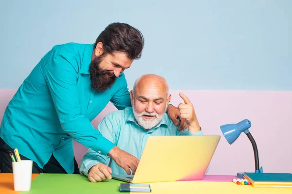 Due impiegati anziani maschi che si consultano con il computer portatile in carica. Conversazione tra colleghi in carica. Gente d'affari che si riunisce intorno a tavolo in ufficio a colori moderno . — Foto Stock