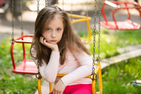 Lekplats. Ett litet barn som svingar. Uttråkad utmattad kvinna i parken. Vacker dag för söt liten flicka i parken. — Stockfoto