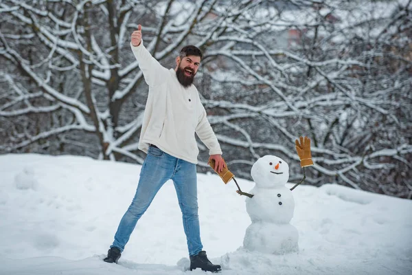 Lustiger Weihnachtsmann posiert bei Winterwetter. fröhliche gut aussehende junge Hipster, die sich mit Schneemann im Winterpark vergnügen. Frohe Weihnachten und ein gutes neues Jahr. — Stockfoto
