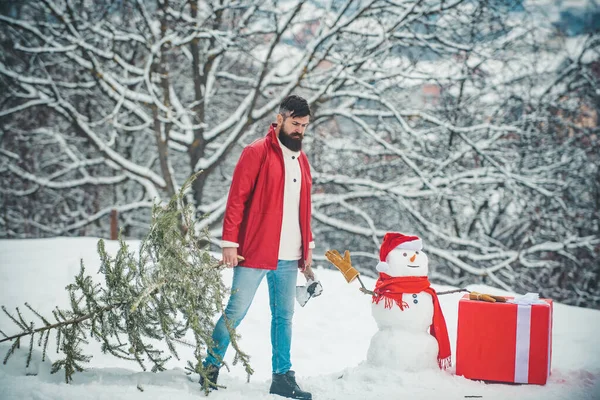 Le jeune bûcheron porte un sapin sur fond de neige blanche. Portrait d'hiver du bois d'oeuvre dans la neige Jardin coupe arbre de Noël . — Photo