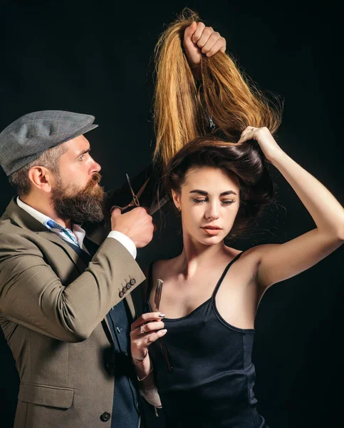 When my hair is long I go to hairdresser. Professional hairdresser and sexy woman. Bearded man ladies hairdresser at work. Hipster holding long hair of pretty woman and hair cutters, hairdresser tool — ストック写真