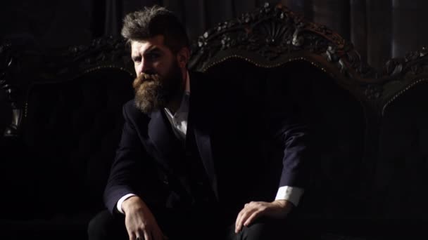 Миллионер в элегантном костюме сидит на роскошном диване. Зрелый мужчина с серьезным лицом в классическом интерьере. Уверенность, успех, стиль, мода, концепция мебели. Жестокий человек или бизнесмен с длинной бородой . — стоковое видео