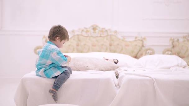 Enfant dans la chambre réglé réveil. Petit garçon avec horloge rétro. C'est l'heure de dormir. Enfant garçon avec un réveil dans les mains s'assoit sur un lit dans la chambre. Quelle heure est il . — Video