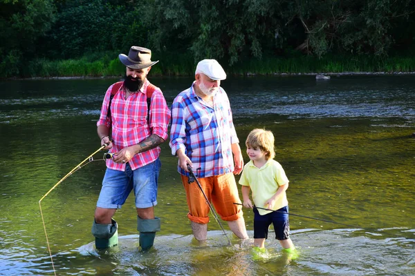 Old and young. Young - adult concept. Fly fishing for trout. Little boy on a lake with his father and grandfather. Father teaching son how to fly-fish in river.